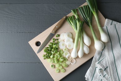 Photo of Board with knife, whole and cut spring onions on grey wooden table, flat lay. Space for text