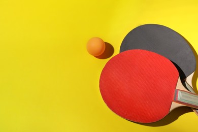 Photo of Ping pong ball and rackets on yellow background, flat lay. Space for text