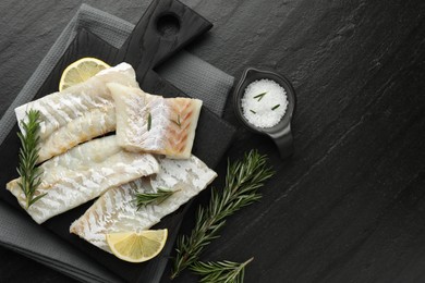 Photo of Fresh raw cod fillets, rosemary, lemon and salt on black table, flat lay. Space for text