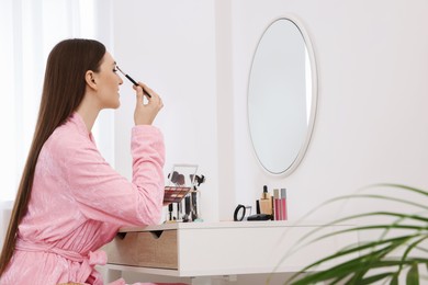 Woman applying makeup with brush at dressing table indoors. Space for text