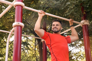 Young man with wireless headphones listening to music while exercising on sports ground