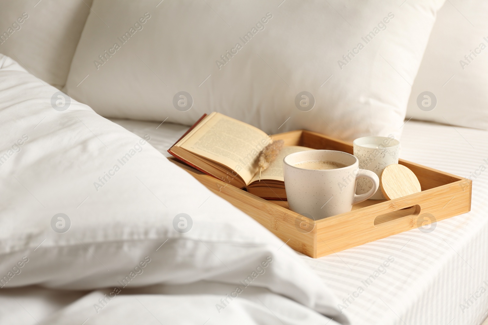Photo of Cup of aromatic coffee, book and candle on bed with soft blanket indoors