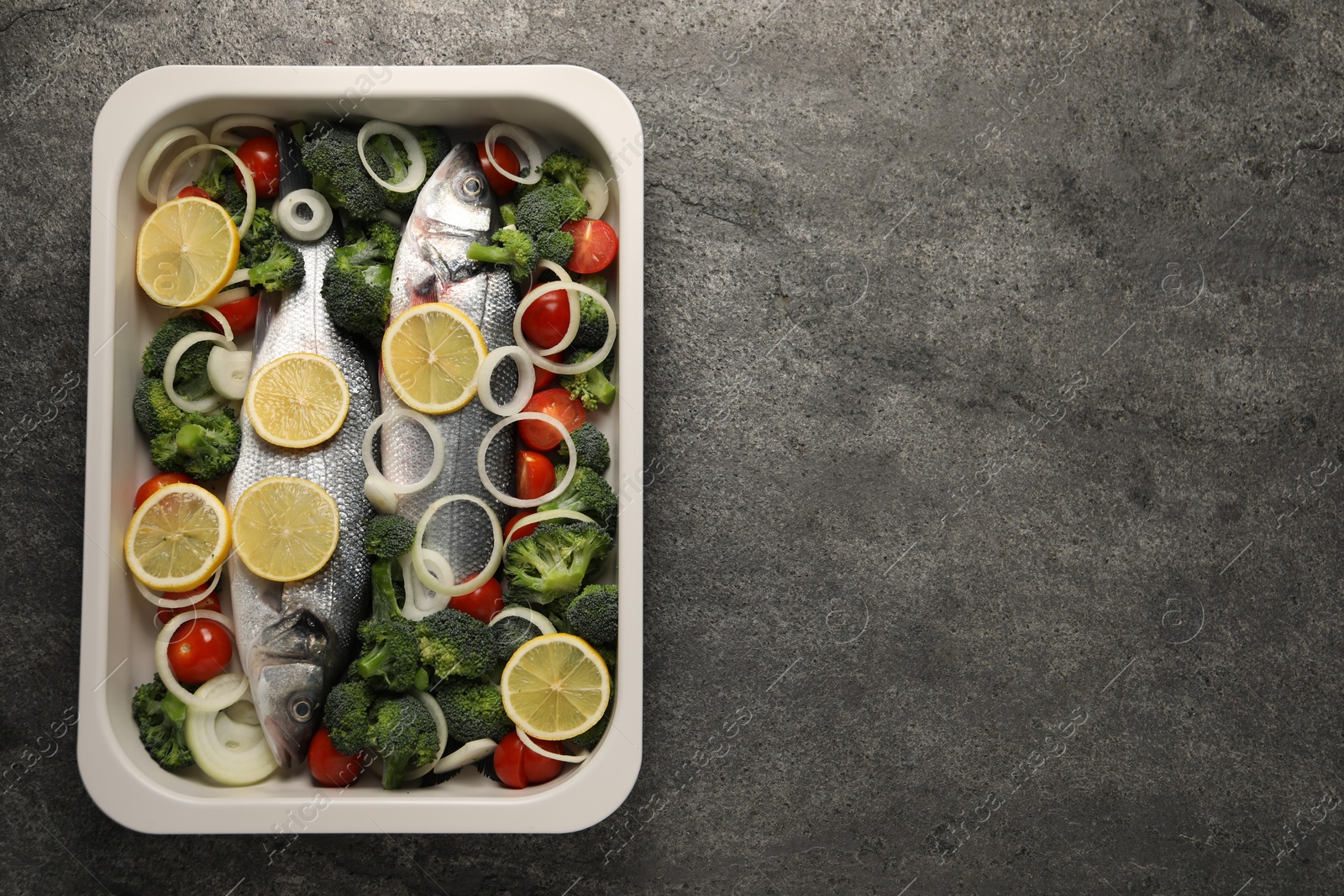 Photo of Raw fish with vegetables and lemon in baking dish on grey textured table, top view. Space for text