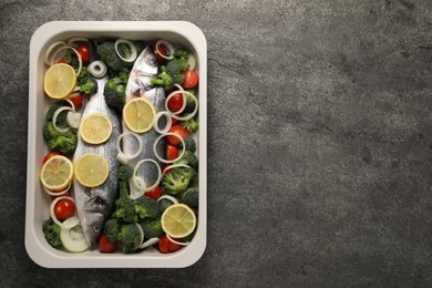 Raw fish with vegetables and lemon in baking dish on grey textured table, top view. Space for text