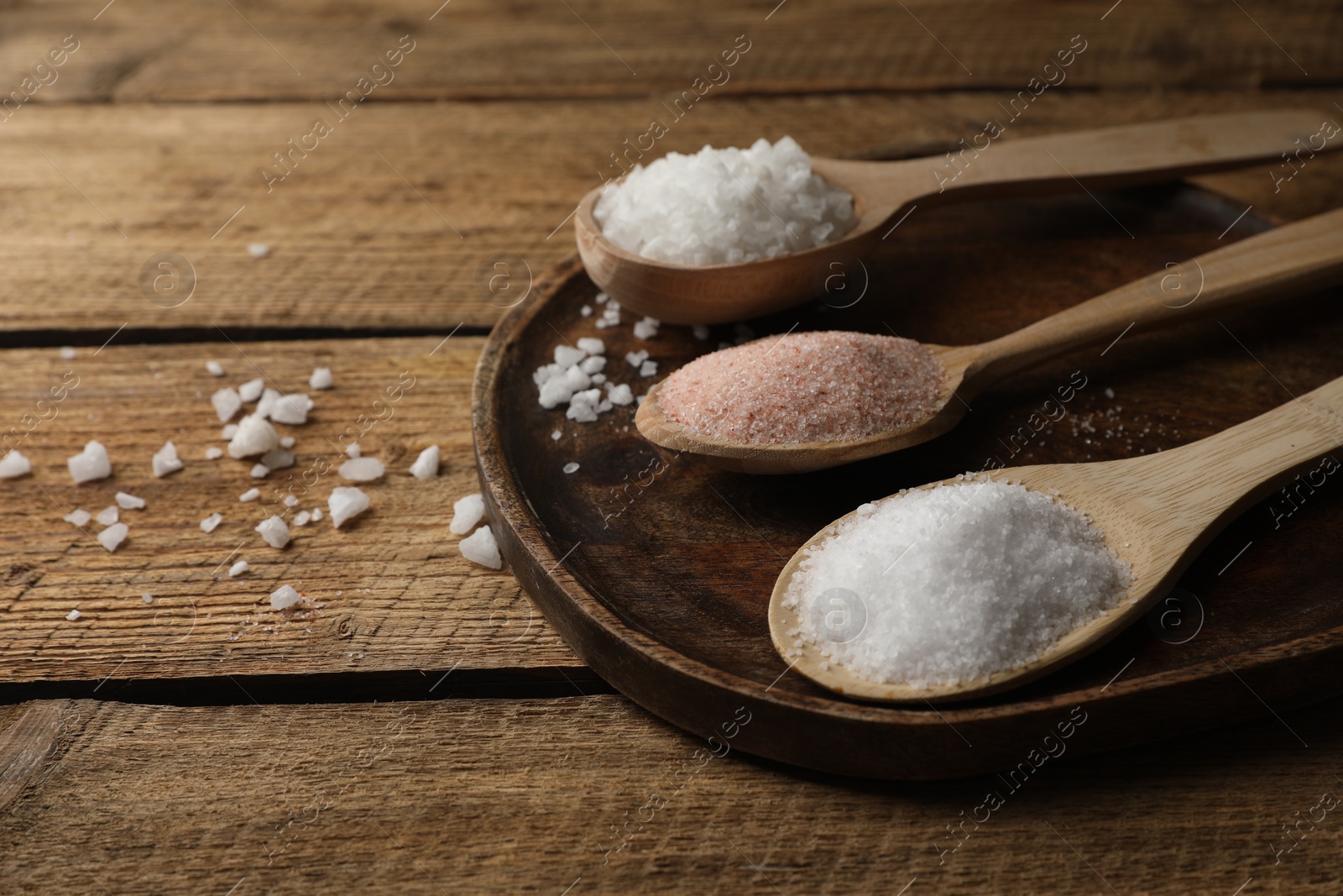 Photo of Different natural salt in spoons on wooden table. Space for text