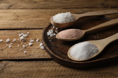 Photo of Different natural salt in spoons on wooden table. Space for text