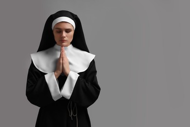 Photo of Nun with clasped hands praying to God on grey background. Space for text