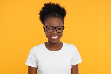 Portrait of happy young woman in eyeglasses on orange background