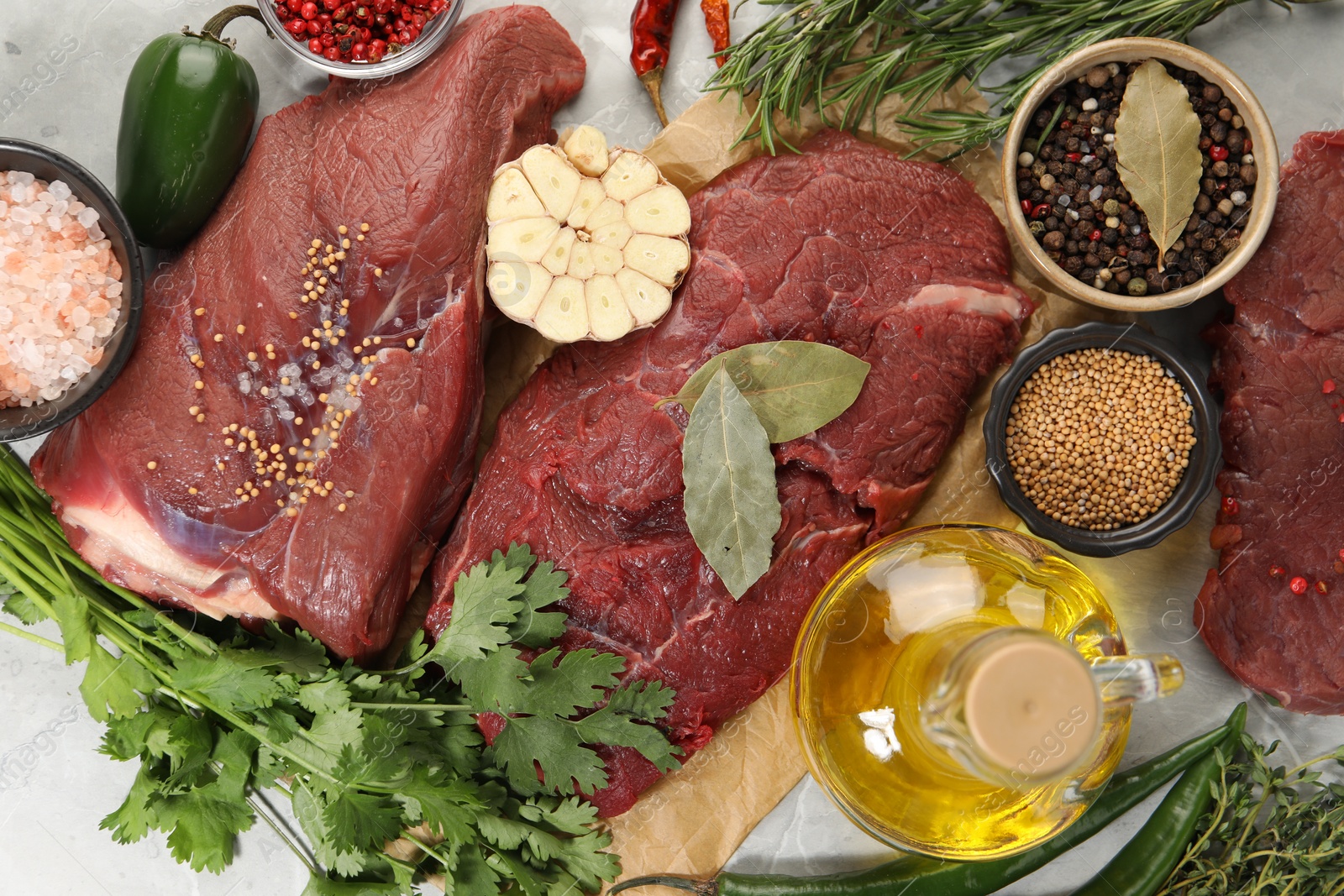 Photo of Pieces of raw beef meat, herbs and spices on light grey table, flat lay