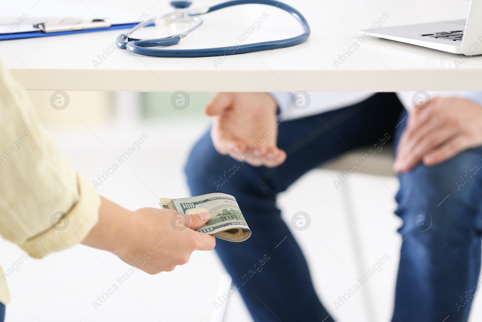 Photo of Patient giving bribe to doctor under table in clinic, closeup. Corrupted medicine