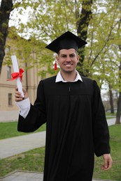 Photo of Happy student with diploma after graduation ceremony outdoors