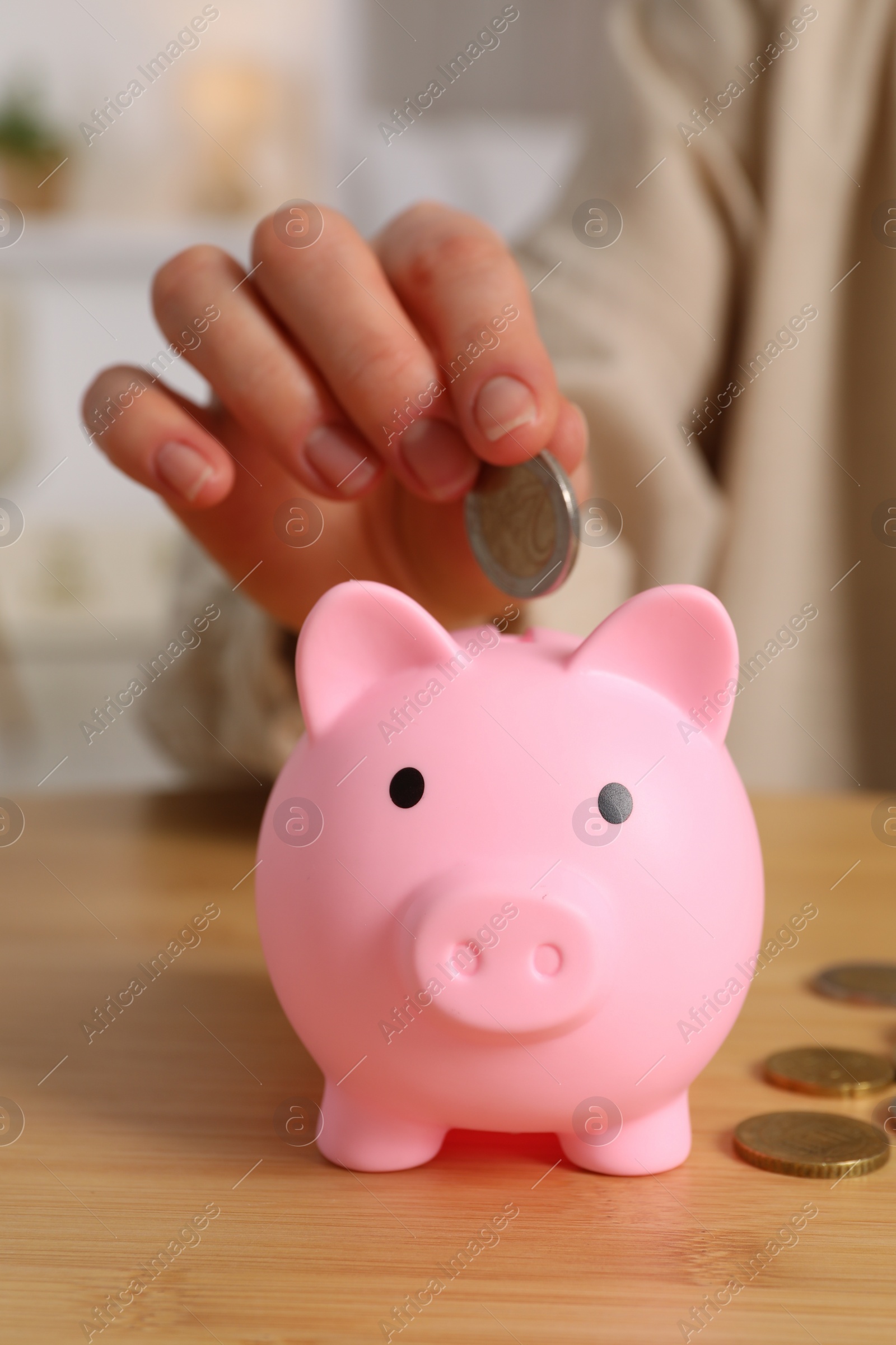 Photo of Woman putting coin into pink piggy bank at wooden table, closeup