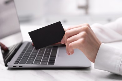 Photo of Woman with laptop holding blank business card at white table, closeup. Space for text