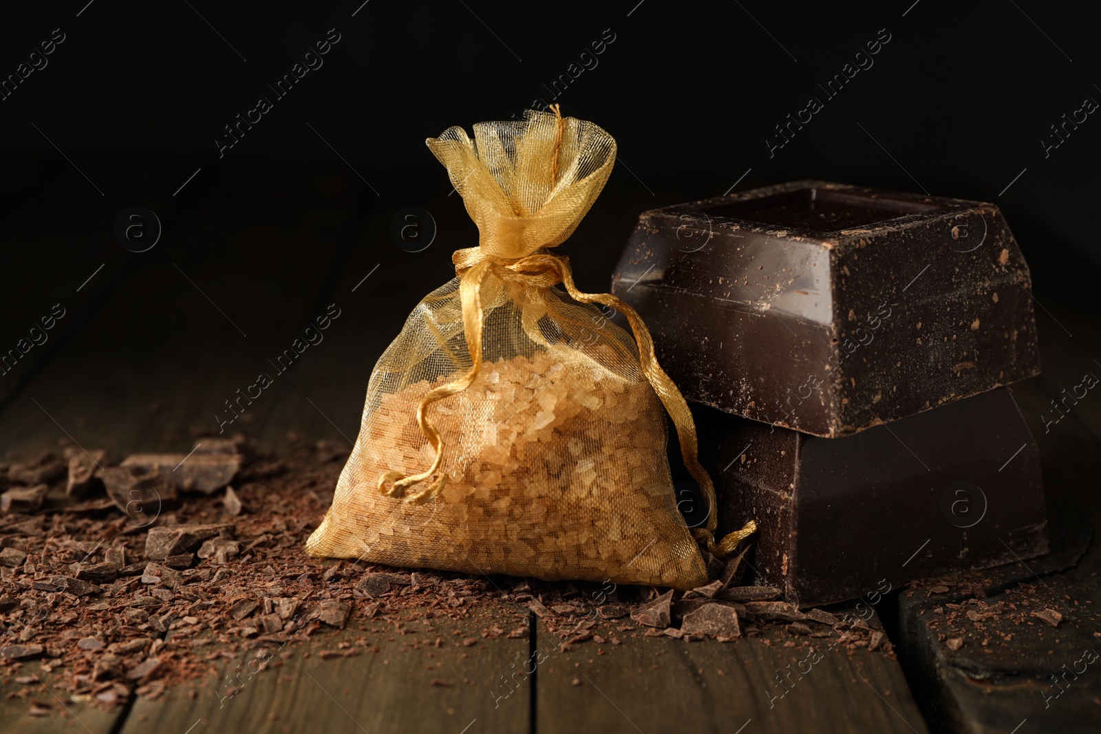Photo of Scented sachet with aroma beads and dark chocolate on wooden table, closeup