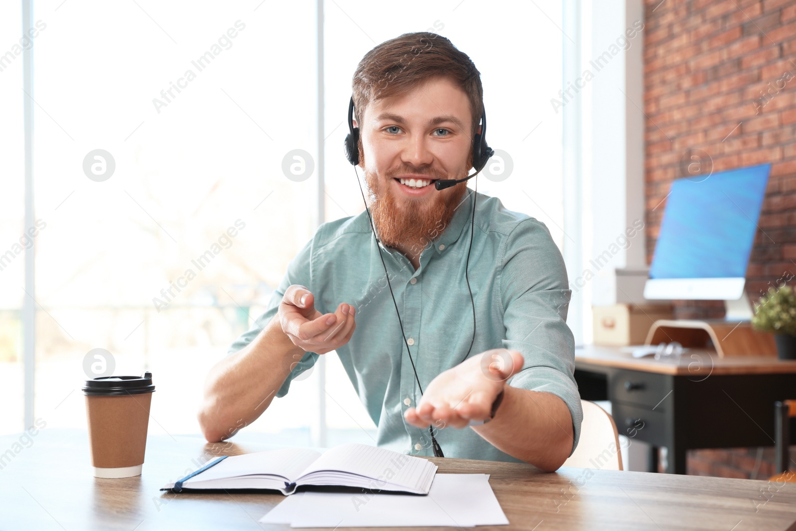 Photo of Young man with headset looking at camera and using video chat in home office