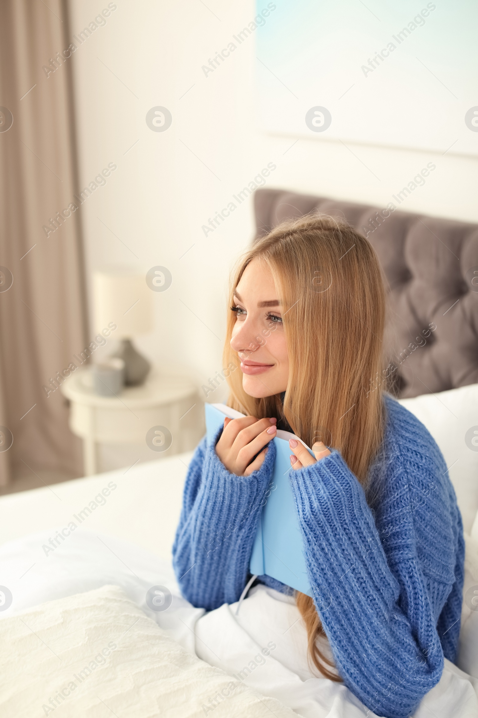 Photo of Beautiful young woman sitting with book in bed and dreaming at home. Winter atmosphere