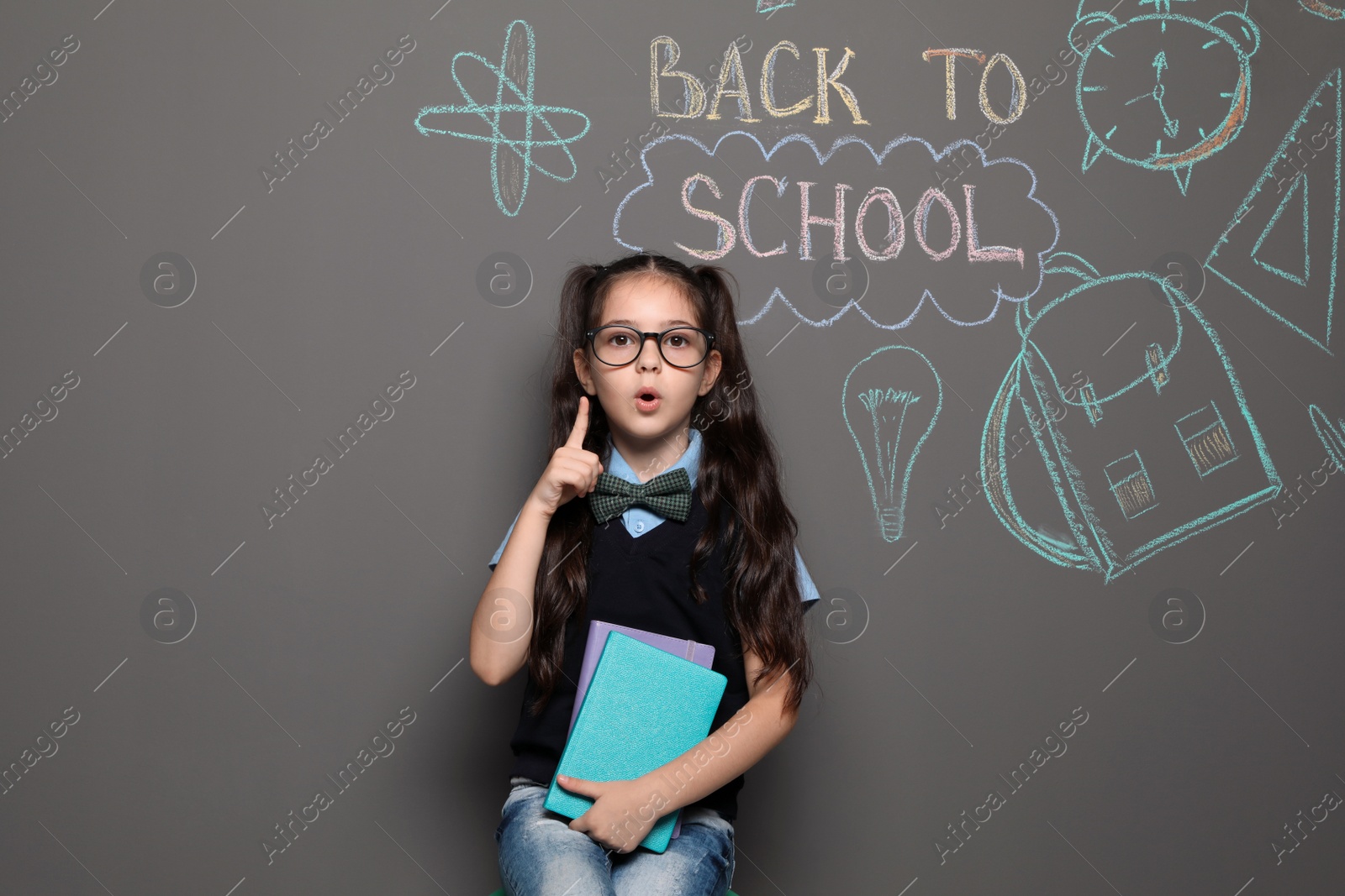 Photo of Little child in uniform near drawings with text BACK TO SCHOOL on grey background