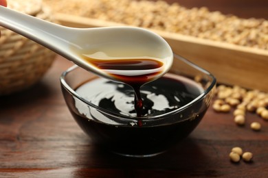 Photo of Taking soy sauce with spoon from bowl at wooden table, closeup