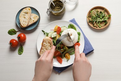 Photo of Woman eating delicious burrata salad at white wooden table, top view