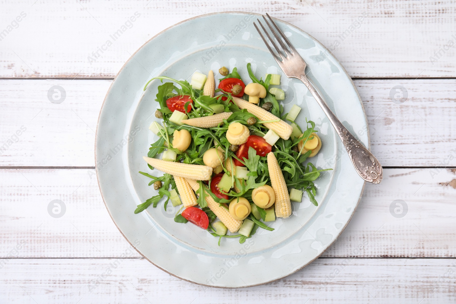 Photo of Tasty baby corn with vegetables, arugula and mushrooms on white wooden table, top view