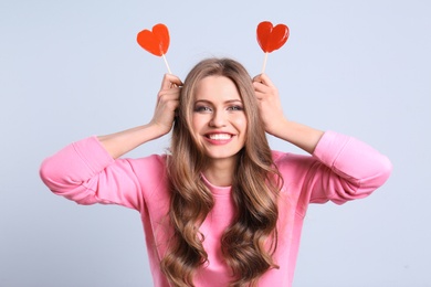 Portrait of young woman with long beautiful hair and lollipops on color background