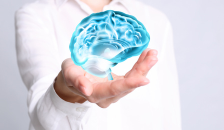 Young woman holding digital image of brain in palm on white background, closeup