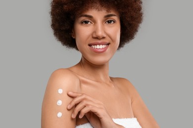 Beautiful young woman applying body cream onto arm on grey background