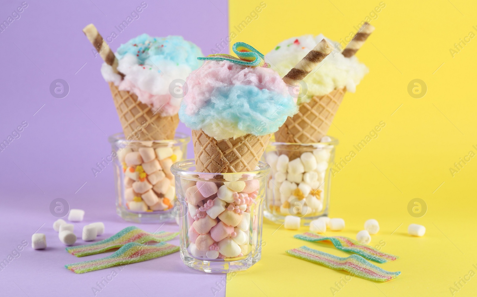 Photo of Sweet cotton candies in waffle cones and marshmallows on color background, closeup