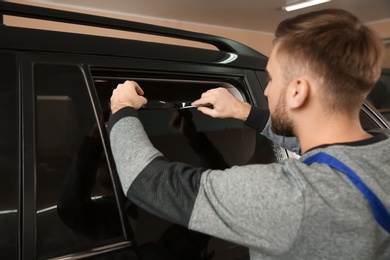 Skilled worker tinting car window in shop