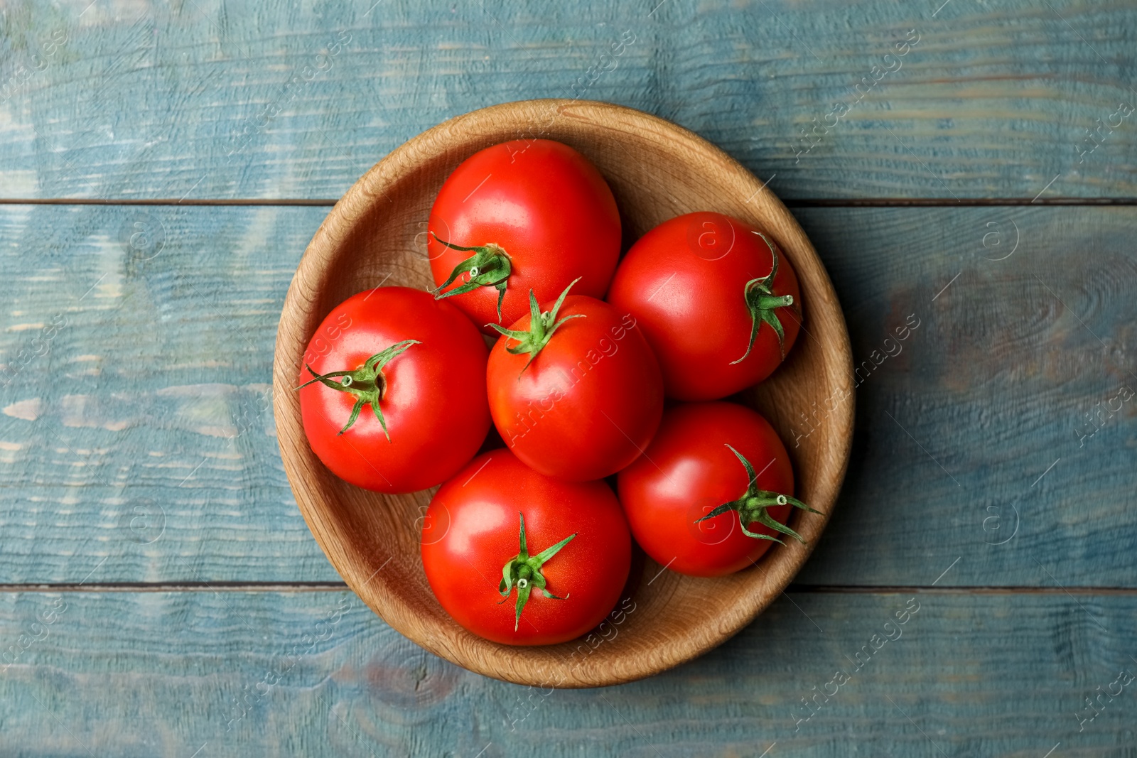 Photo of Ripe tomatoes in bowl on blue wooden table, top view