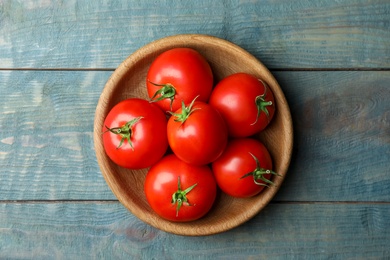 Ripe tomatoes in bowl on blue wooden table, top view