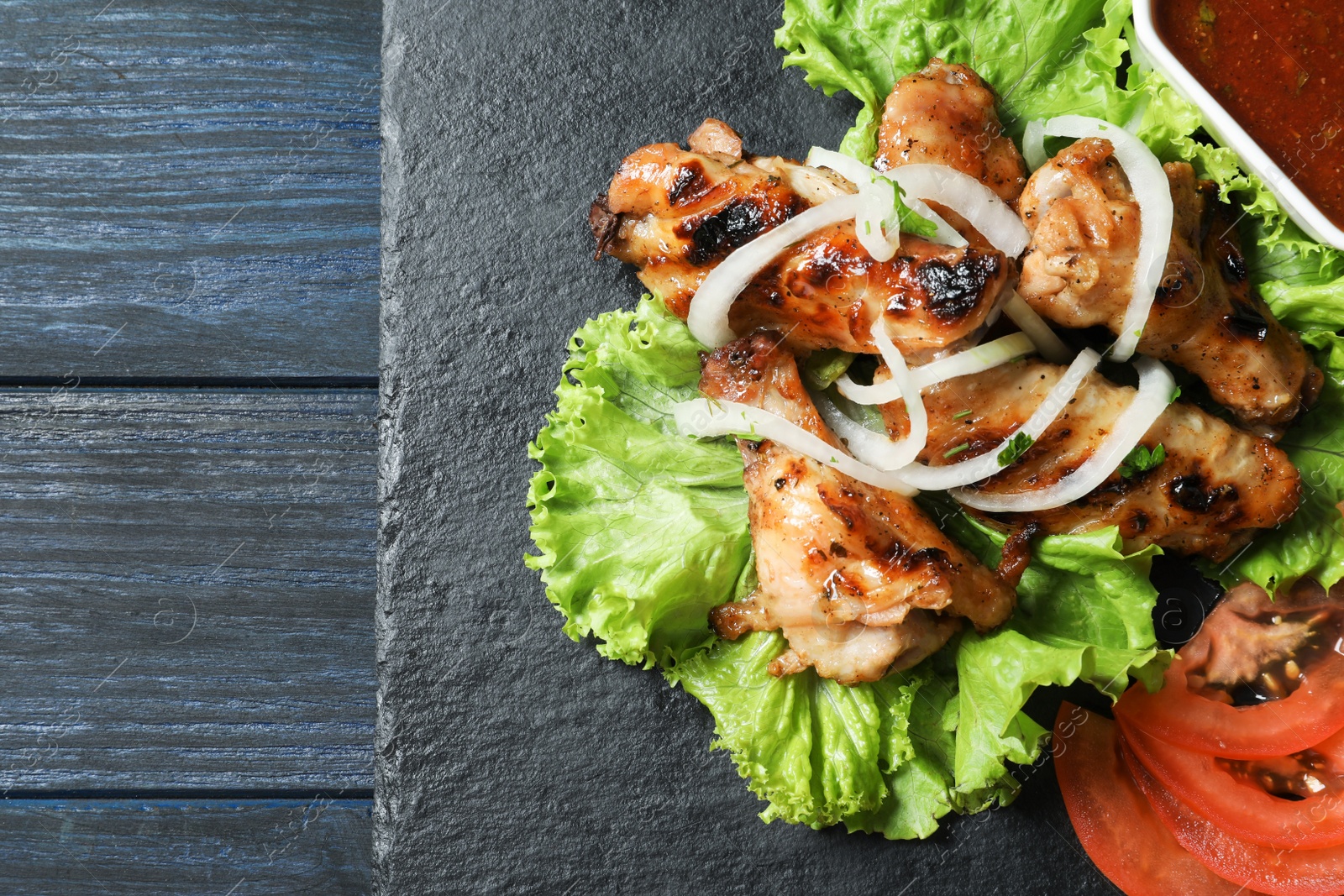 Photo of Slate plate with tasty shish kebab and sauce, top view