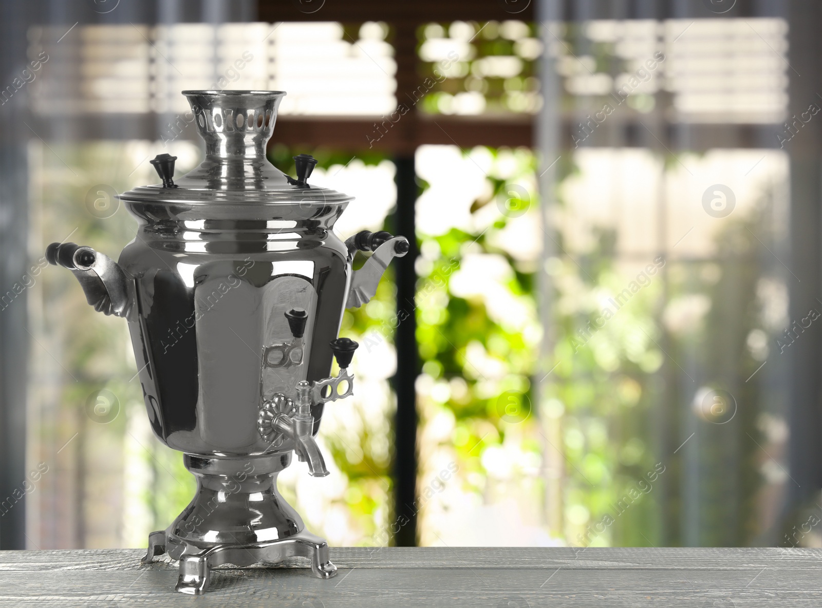 Image of Traditional Russian samovar on wooden table against window in room. Space for text