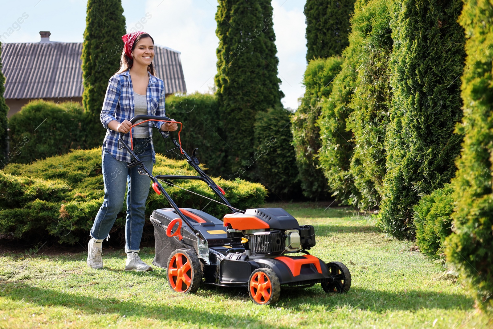 Photo of Smiling woman cutting green grass with lawn mower in garden