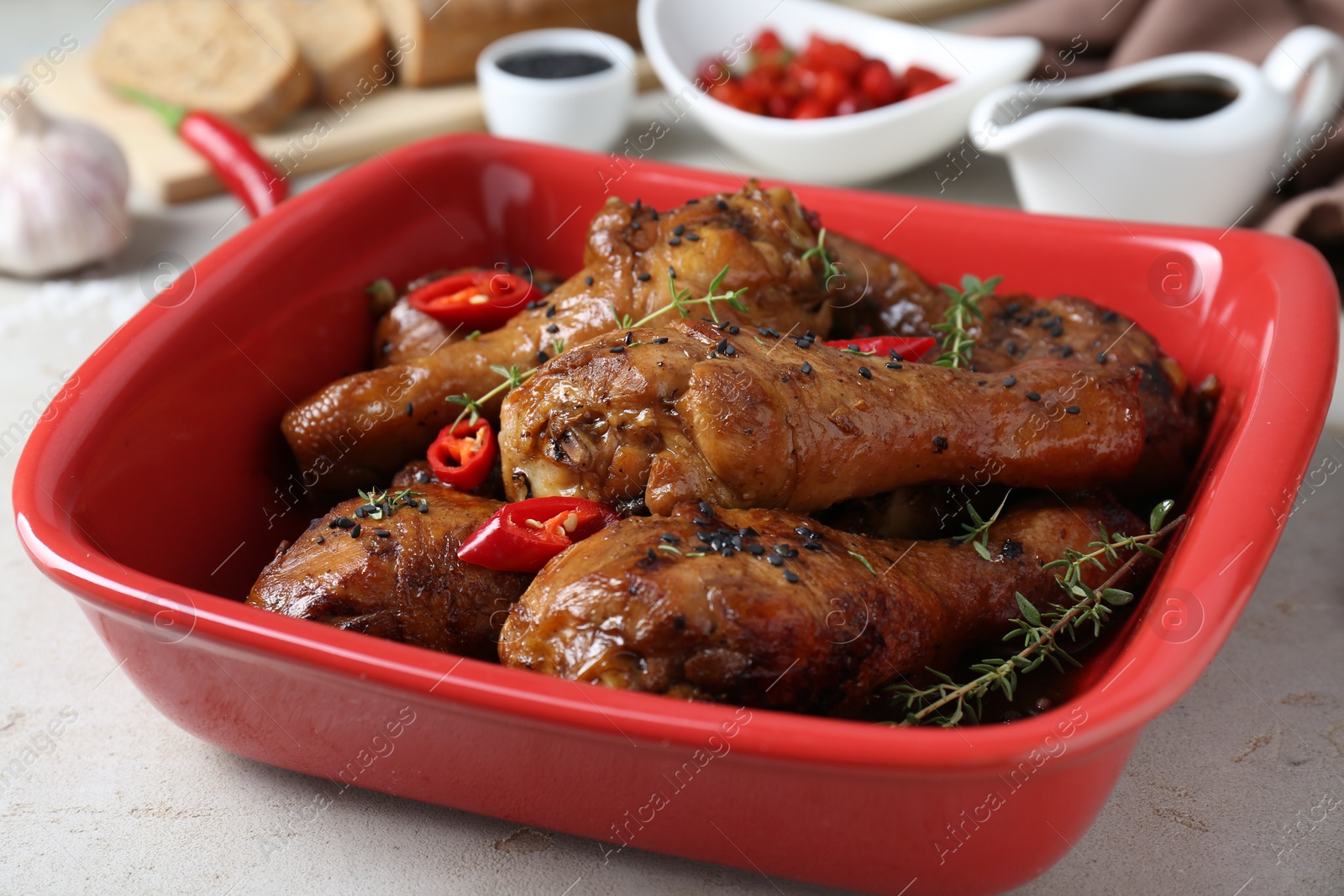 Photo of Chicken legs glazed in soy sauce with black sesame, chili pepper and thyme on light table, closeup