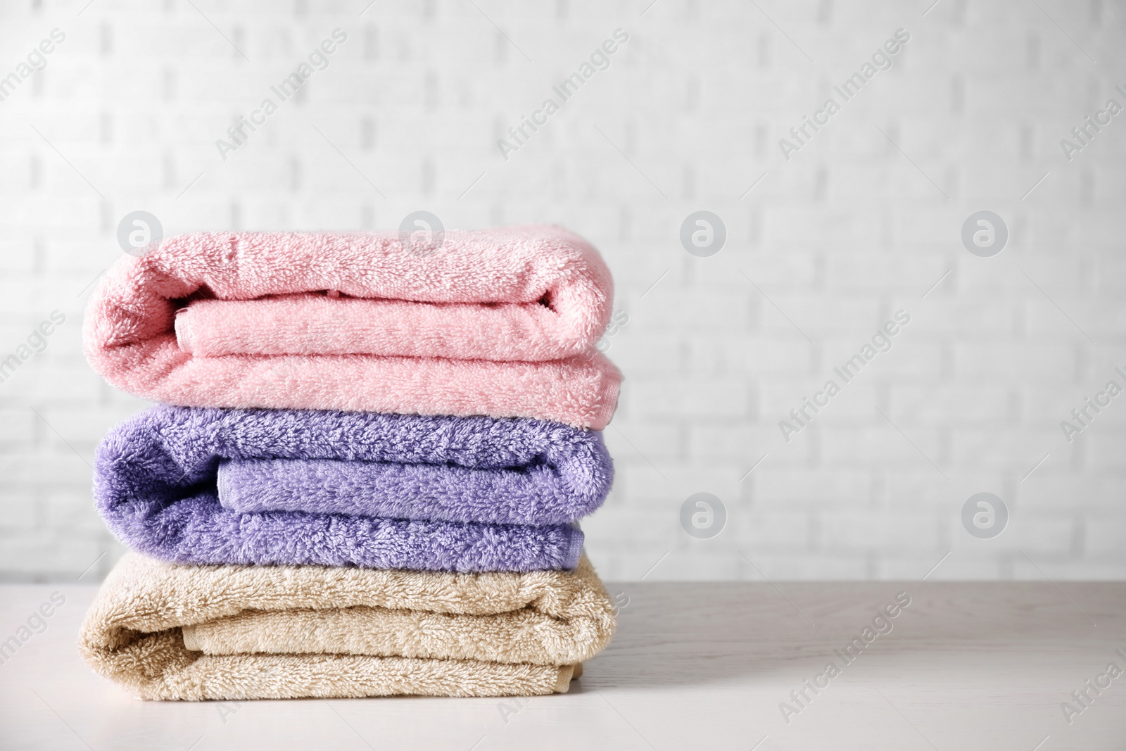 Photo of Stack of clean bath towels on white wooden table. Space for text