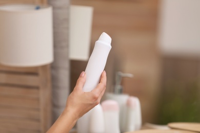 Photo of Young woman holding deodorant in bathroom, closeup