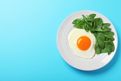 Plate of fried egg and spinach on light blue background, top view with space for text. Healthy breakfast