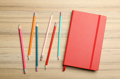 Photo of Stylish red notebook and pencils on wooden table, flat lay