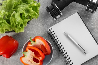 Photo of Healthy diet. Vegetables, dumbbells, notebook and pen on grey table, flat lay