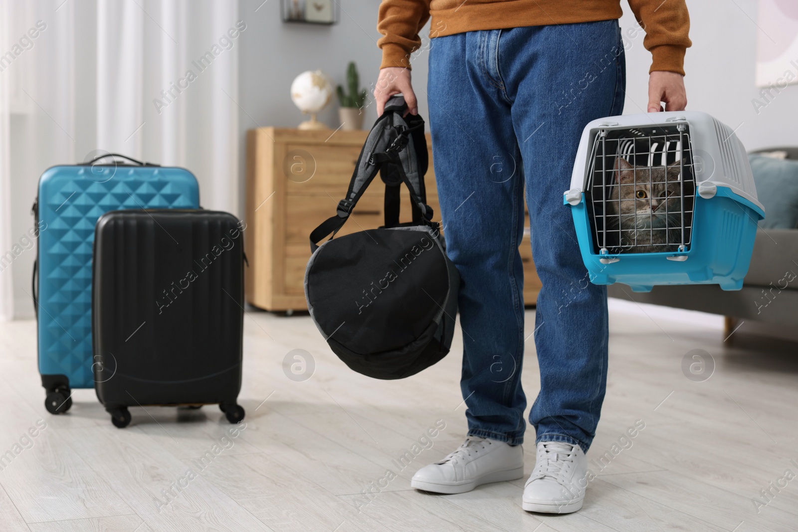 Photo of Travel with pet. Man holding carrier with cute cat and bag at home, closeup