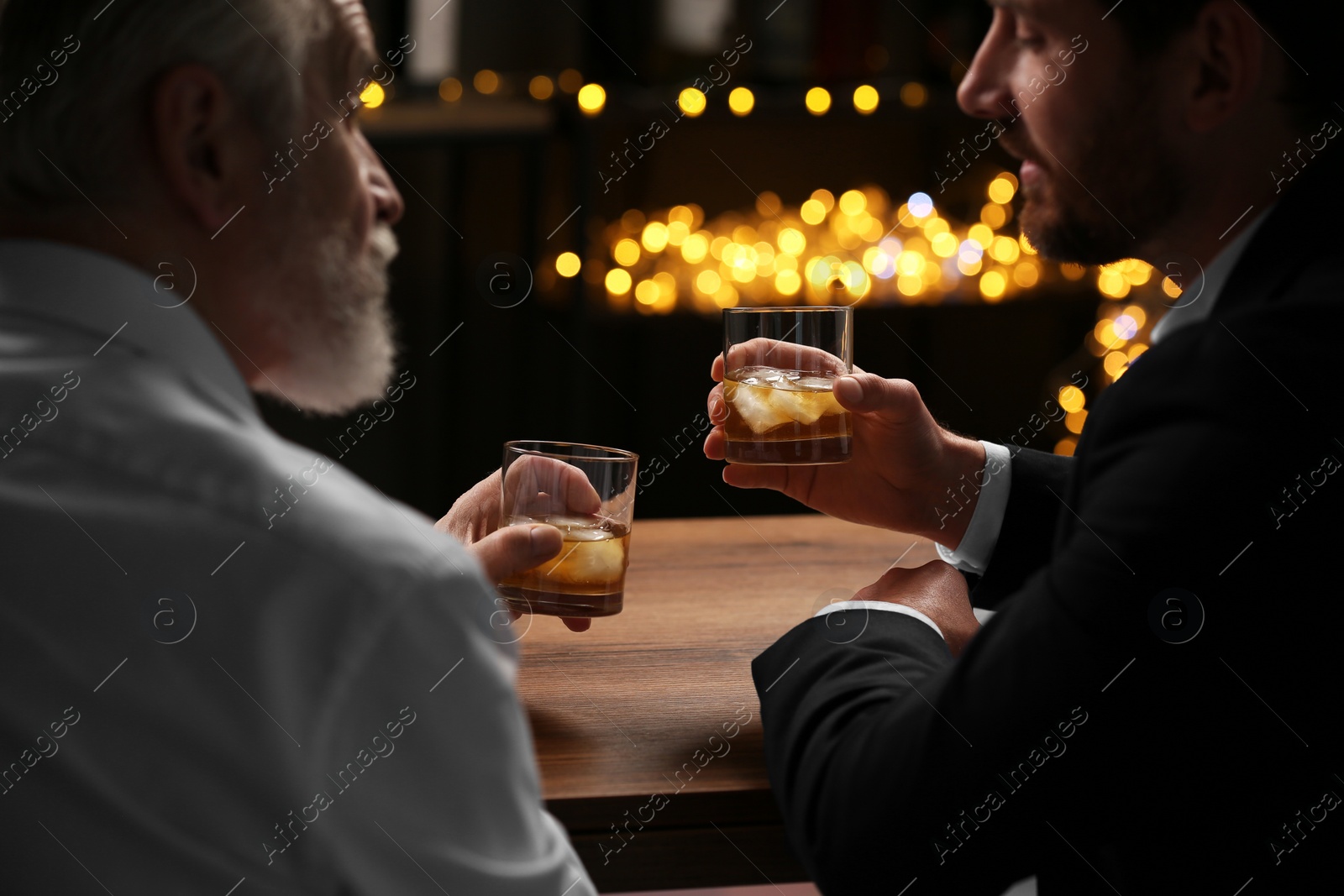 Photo of Men with glasses of whiskey talking at wooden table in bar