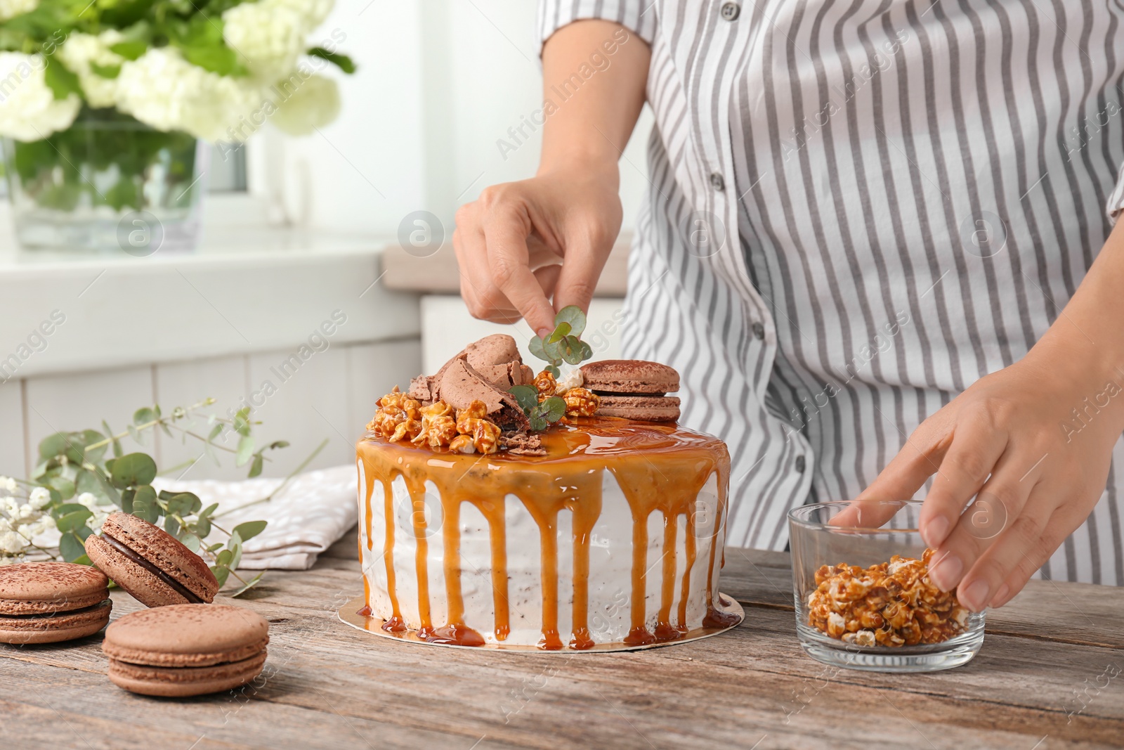 Photo of Young woman decorating delicious caramel cake at table