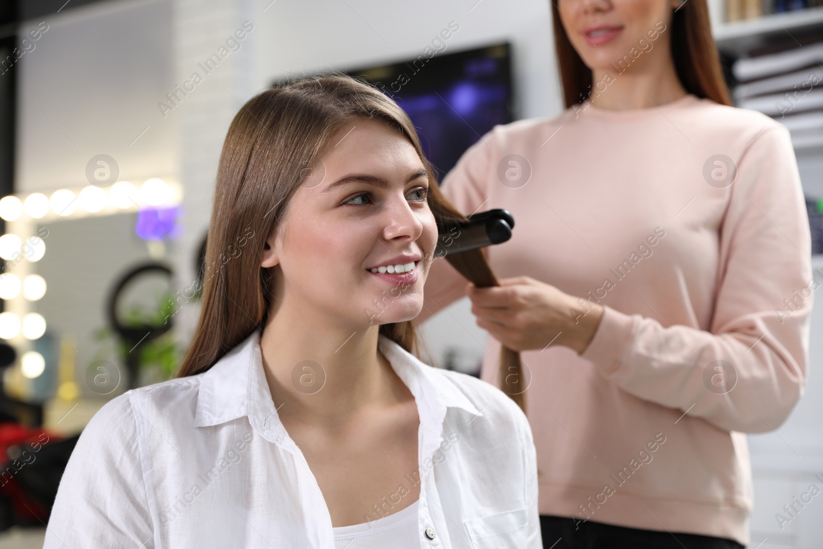 Photo of Hairdresser using straightener to style client's hair in salon