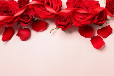 Photo of Beautiful red roses, petals and ribbon on pale pink background, flat lay. Space for text