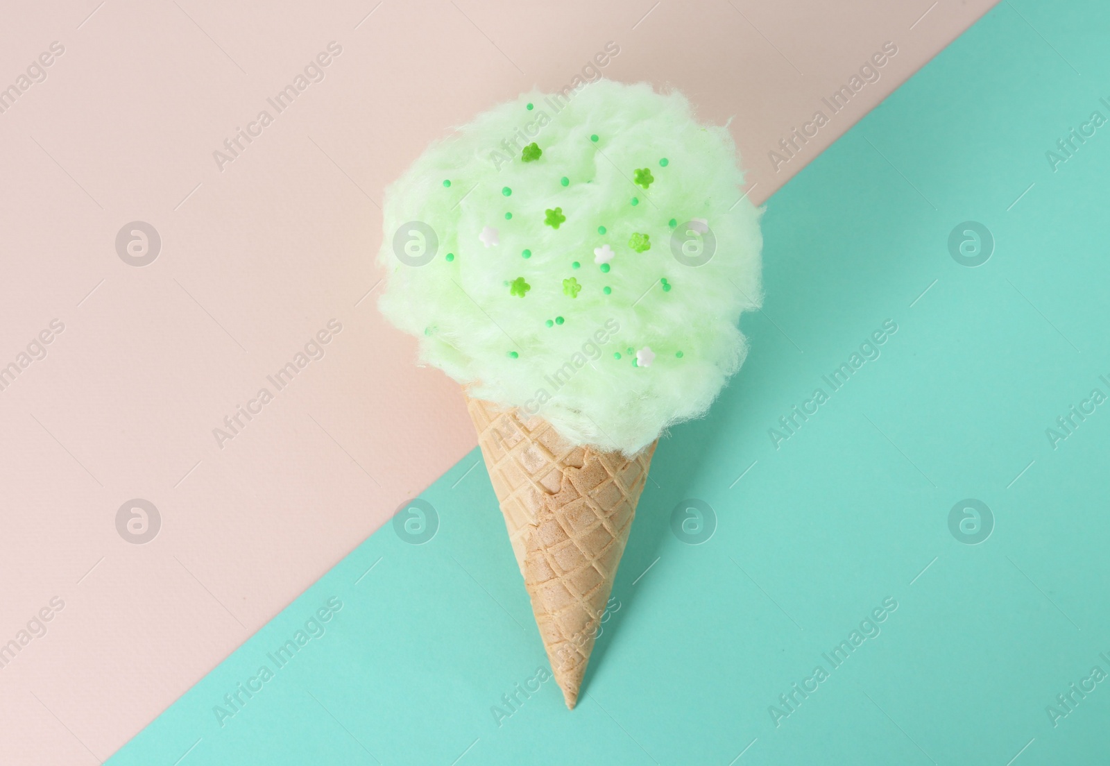 Photo of Sweet cotton candy in waffle cone on color background, top view