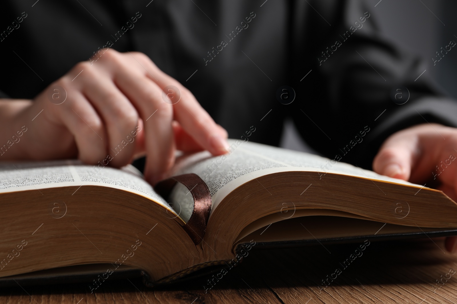 Photo of Closeup of woman reading Bible at wooden table, focus on book