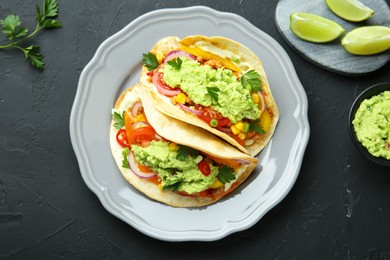 Delicious tacos with guacamole and vegetables served on black table, flat lay