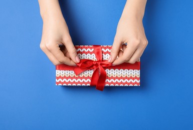 Photo of Woman decorating gift box on blue background, top view. Christmas present