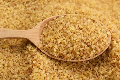 Photo of Wooden spoon on pile of uncooked bulgur, closeup